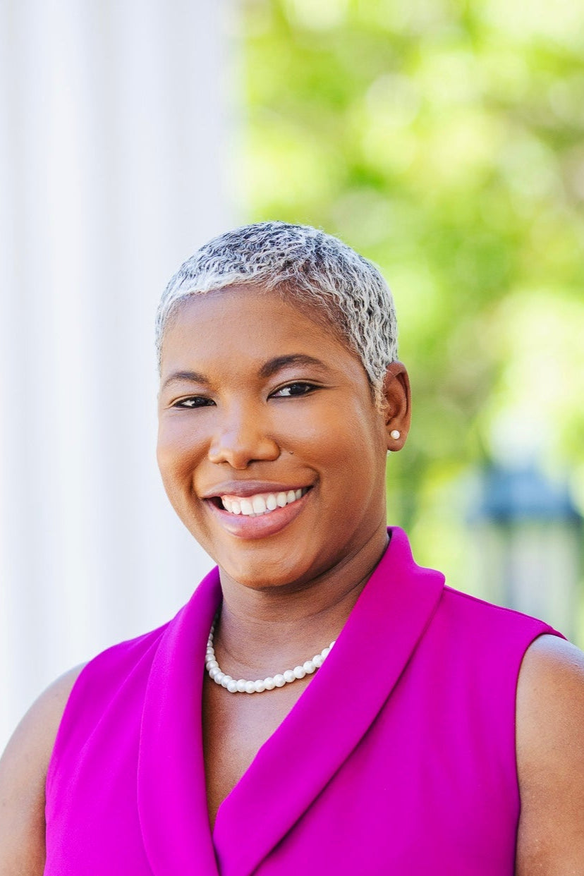 Woman in a bright pink outfit standing outdoors with blurred greenery in the background